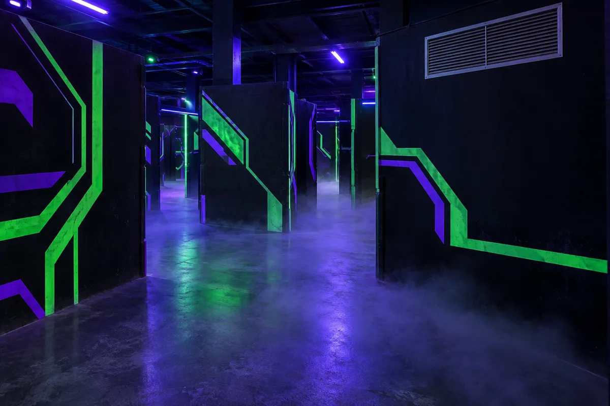Arène de laser game vide en lumière noire, cloisons peintes et grille de ventilation en partie haute