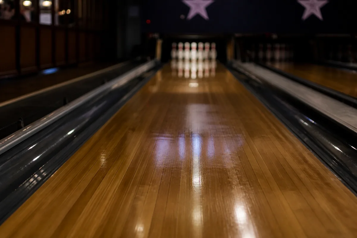 Piste de bowling vue depuis la zone d&rsquo;élan, reflets d&rsquo;huile visibles sur le vernis