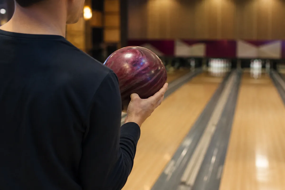 Joueur de bowling immobile en position de départ, boule tenue à hauteur de poitrine, salle en arrière-plan