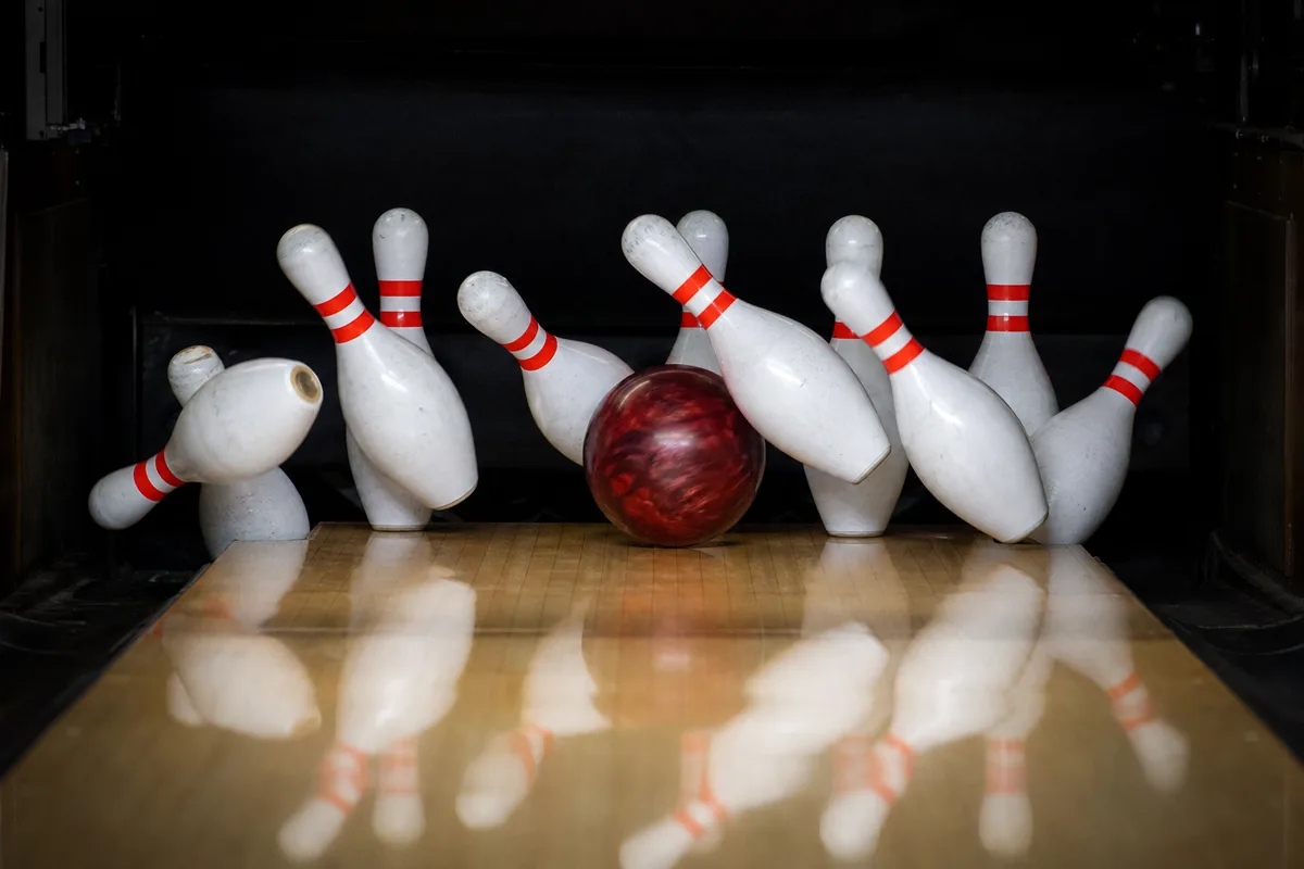 Boule de bowling frappant les quilles dans la zone du pocket, quilles projetées en pleine action